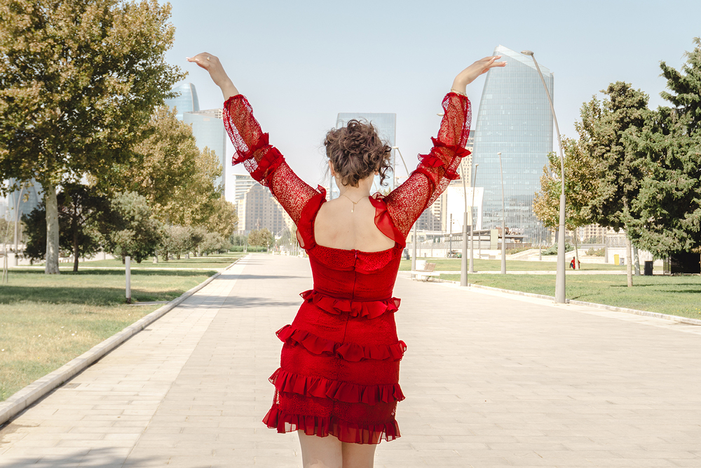 A young woman posing confidently in a modern urban environment, showcasing contemporary fashion, natural beauty, and a vibrant city lifestyle with stylish architecture in the background.
