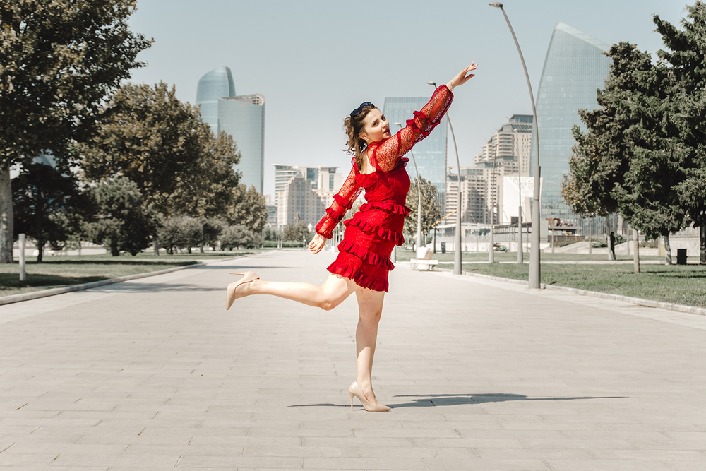 A young woman posing confidently in a modern urban environment, showcasing contemporary fashion, natural beauty, and a vibrant city lifestyle with stylish architecture in the background.
