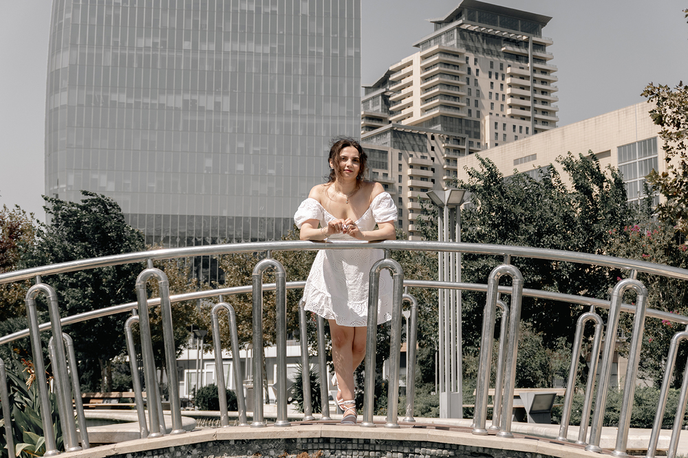 A young woman posing confidently in a modern urban environment, showcasing contemporary fashion, natural beauty, and a vibrant city lifestyle with stylish architecture in the background.
