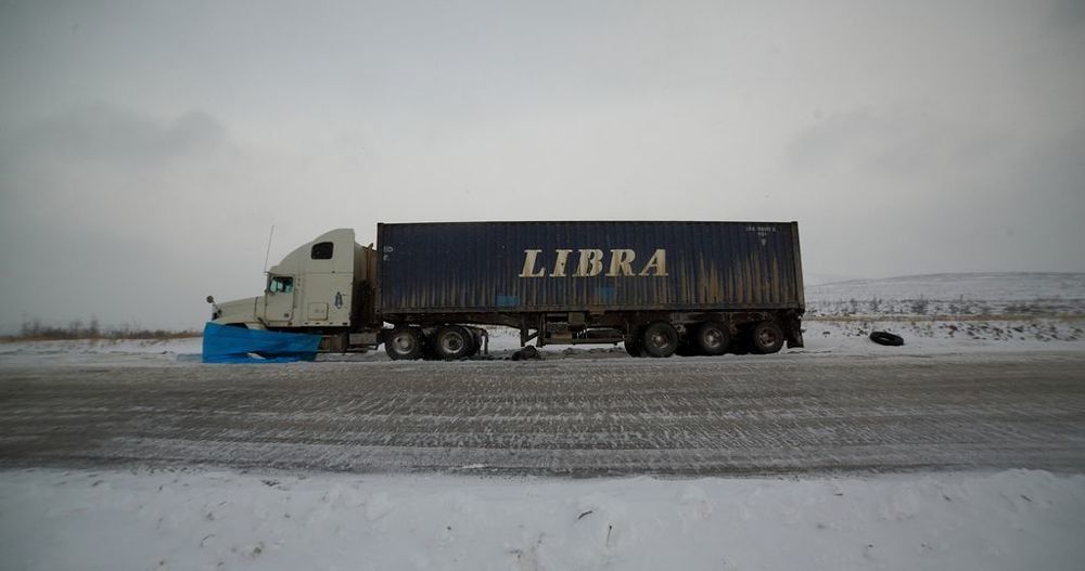 БЕЗ МАТА НЕ ПРОЕДЕШЬ  Почти от самого Алдана я на своей машине протискивался среди застрявших большегрузов, включив все свои WD and Lock. Мой внедорожник справился с трассой с большим трудом. На протяжении всего участка пути над тайгой висит могучий мат. Цензурные в речи дальнобойщиков только предлоги.  На самом перевале &mdash; фура. &laquo;Морда&raquo; закрыта китайским синим пологом. Стучу в кабину: мол, как дела? Никак не ожидал что ответ мне &laquo;прилетит&raquo; из-под задних колес грузовика:  &mdash; Здорово, мужик! Кинь ключ на 24 и во-о-он ту монтажку маленькую.  Отыскав у колеса почти засыпанные снегом ключи и монтажку, пытаюсь понять, куда и кому их подать. Между колес появляется рука без перчаток: &laquo;Давай сюда&raquo;.   Сергей, водитель из Благовещенска, выполняет рейс на Якутск.  &mdash; Давно стоишь?  &mdash; Третий день. Задний мост накрылся, прям на подъеме завыл, и я встал. Спасибо дорожникам, затащили наверх быстро трактором в сцепке с грейдером. Скоро ребята должны подъехать, привезти запчасти. Хорошо, телефон тут берет, если б не связь, то торчал бы еще дольше. Главное, сегодня все сделать, а то у меня уже солярки совсем мало осталось.  Выскакивает из-под машины:  &mdash; Слушай, а у тебя вода есть? Пойдем, чаю попьем, как раз погреюсь, и поговорим уже в тепле.   Иду в свою машину за водой, прихватываю конфеты и печенье. В кабине Сергея газовая плитка, чайничек, кружки &mdash; уже все готово к моему приходу. Сергей, быстренько налив воды, разжег плитку, по пути закидывая в рот печенье и заедая конфетой, начал рассказывать, что вчера, сняв сломанную запчасть уже совсем впотьмах, не заметил, что повреждена еще и полуось. Поругал фонарик &mdash; на морозе совсем уже не светит. Поведал, что машина не его, и в рейс он поехал подменить друга, ну и, естественно, досталось дорожникам, власти, олигархам, яхтам и пальмам на Майорке. Задаю вопрос уже в лоб: &laquo;Серега, ты что так печенье метешь?&raquo;. Оказалось, что провизия у него закончилась сегодня утром, вода из снега, что он топит, очень грязная, и уже болит живот. Я отдал ему еще &laquo;Доширак&raquo;, тушенку, хлеба и консервы.   После ужина Сергей попросил посветить ему фарами, пока не приехали его знакомые. Я притащил из машины фонари и занял &laquo;почетное место&raquo; у колес, подавая ключи.