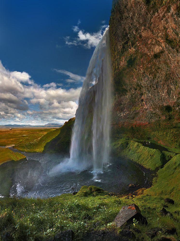 Seljalandsfoss &ndash; очень комфортно-достигаемый 60-метровый водопад расположен рядышком с Исландской кольцевой автомобильной дорогой, километрах в 100 от Рейкьявика. При желании (и не боясь промокнуть) можно пройти прямо за каскадом, чем и заняты заметные на фотке тоуристы