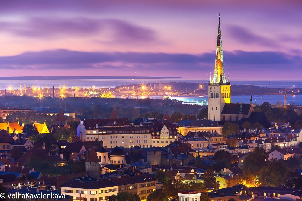 Aerial cityscape with Medieval Old Town illuminated in evening twilight and St. Olaf Baptist Church, sea and port in Tallinn, Estonia