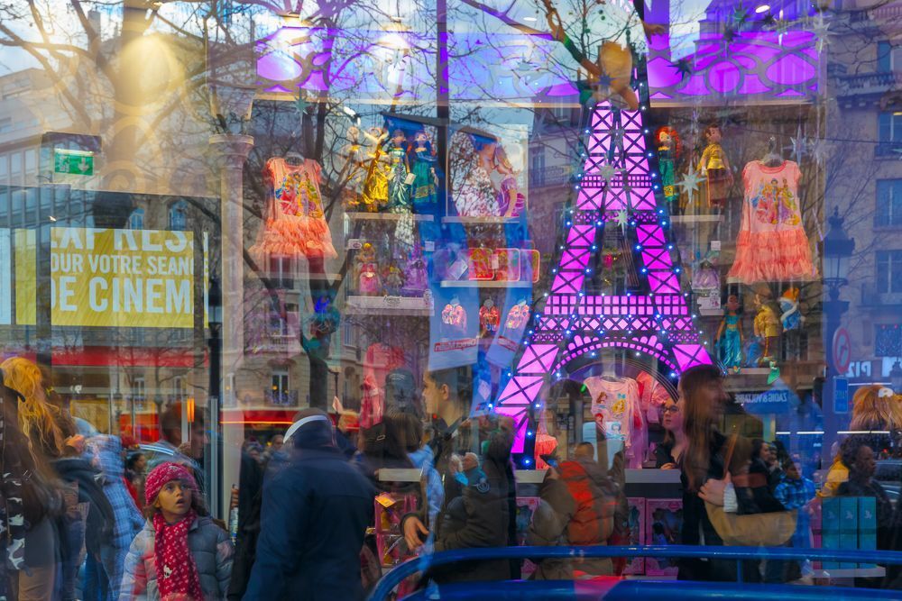 Multi-colored children's shop window with the image of the Eiffel Tower and reflections passers-by and customers in Paris, France