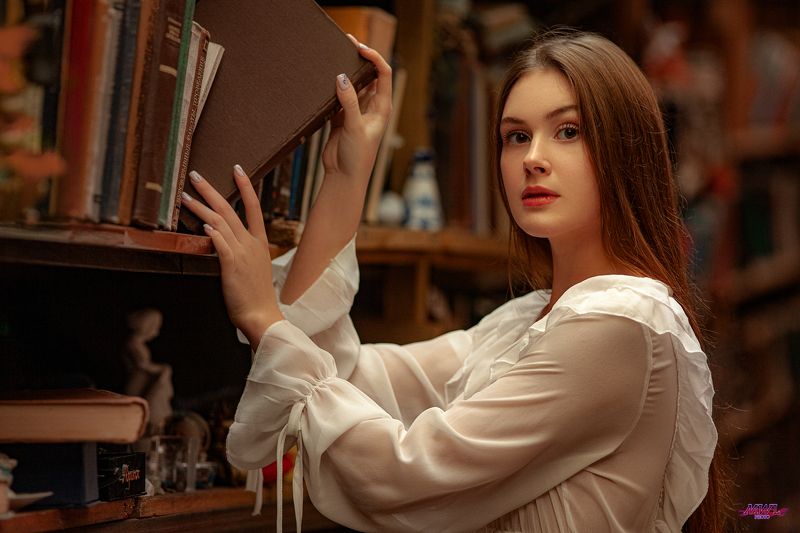 Young woman reading book in library фото превью