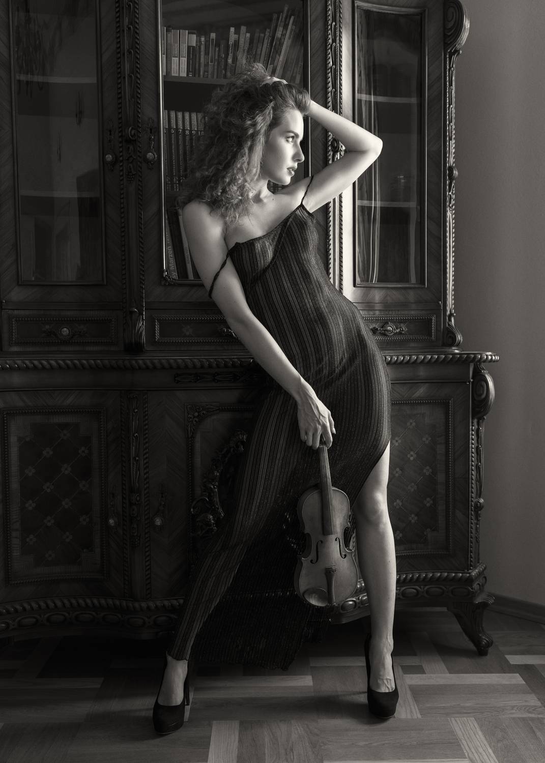 antique furniture, artistic portrait, beautiful woman, bookcase background, dress, elegant pose, femininity, front view, grace, high heels, indoors, monochrome, musical instrument, one person, pensive look, standing, vintage aesthetic, violin, young woman, Alex Tsarfin