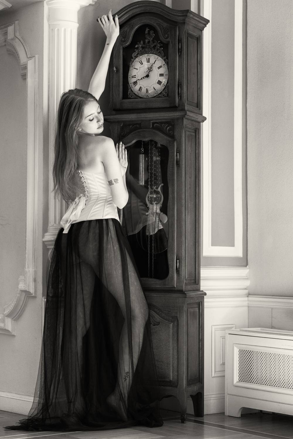 artistic nude, back view, beautiful woman, corset, dark romanticism, elegant pose, feminine grace, grandfather clock, modern muse, monochrome, nostalgic, one person, quiet sensuality, reflection, sheer fabric, standing, vintage aesthetic, young woman, Alex Tsarfin