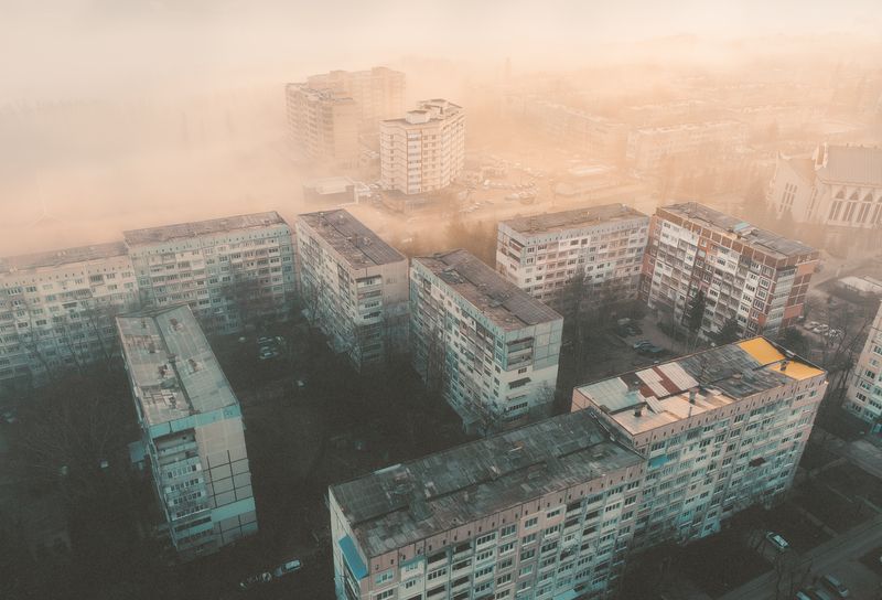 город, урбан, городской пейзаж, спальный район, панельные дома, многоэтажки, архитектура, бетон, двор, крыши, вид сверху, дрон, аэрофото, туман, дымка, пыль, смог, рассвет, утро, оранжевый свет, холодные тона, атмосфера, минимализм, геометрия, индустриаль Город в пыльном тумане фото превью