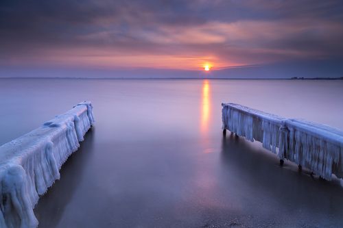 Frozen piers in sea at sunset