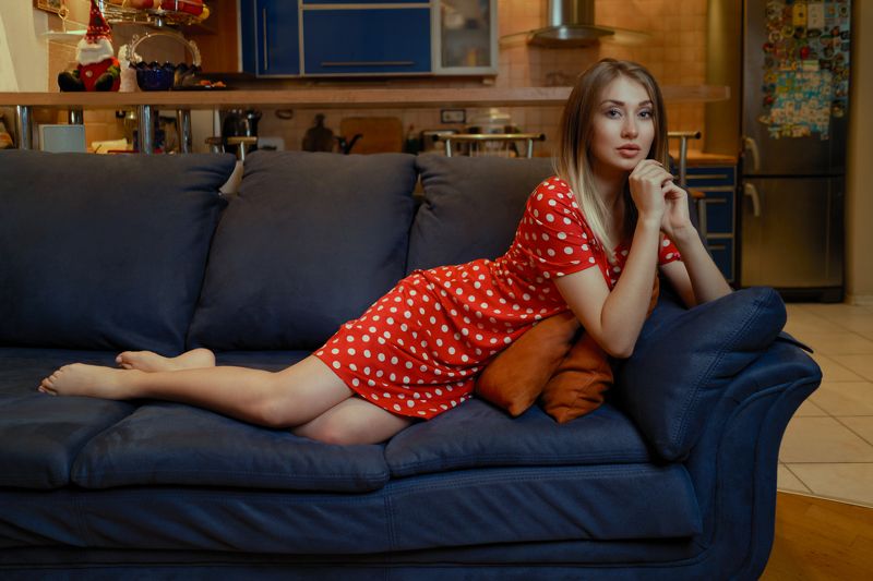 Girl posing on a sofa in a red polka-dot dress in a home studio on the background of the kitchen фото превью